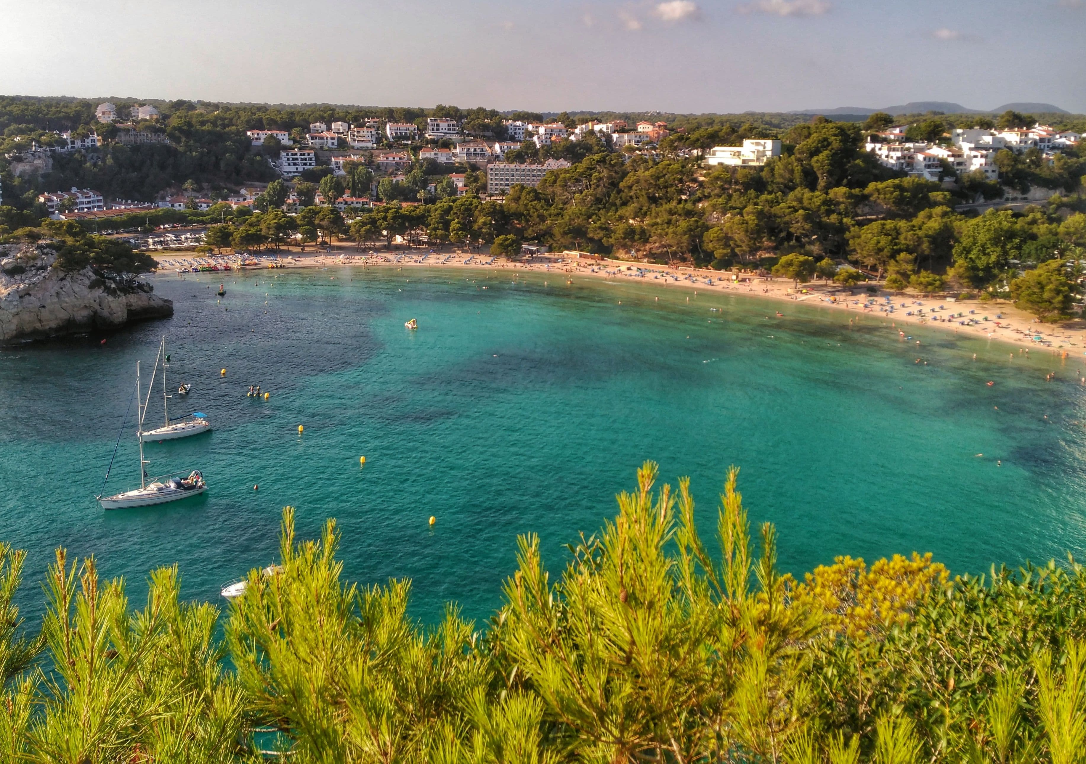 Cala Galdana vista des de la pineda, amb la platja al fons de la cala i velers fondejats en aigua turquesa