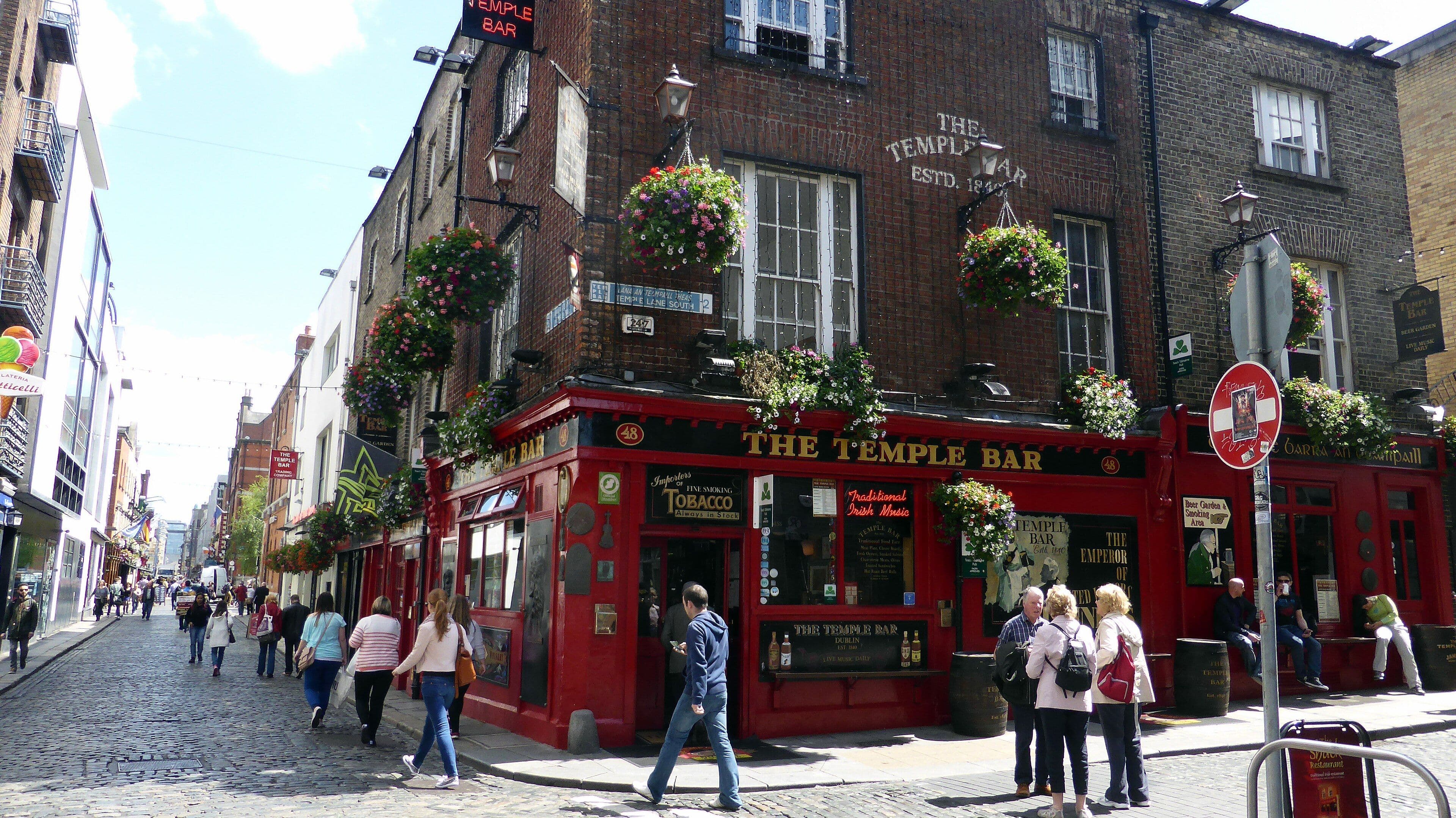 La fachada roja del pub The Temple Bar, con flores en los balcones y gente paseando por la calle empedrada